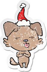 distressed sticker cartoon of a dog sticking out tongue wearing santa hat