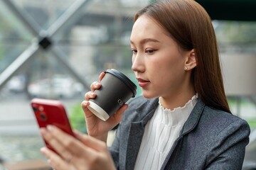 Young asian businesswoman beautiful female lady sitting in a cafe and sipping a cup of coffee calmly and looking at her mobile phone for sales report update from her team