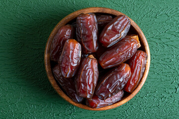Date fruits in wooden bowl,on green background
