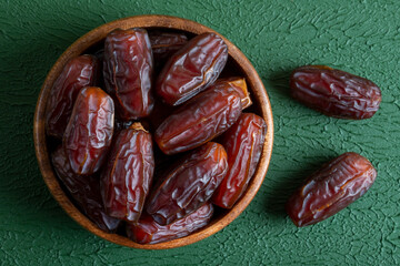 Date fruits in wooden bowl,on green background
