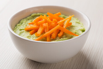 Diet vegetarian avocado soup puree in white bowl on wood table, close up. Slices of bell pepper on top. Healthy vegan food.
