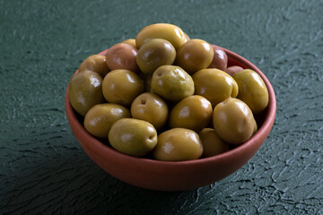 Bowl full of green olives on green background