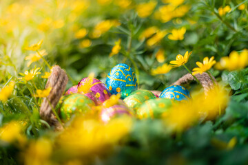 Easter eggs in wicker basket in yellow bright flowers and nature. Traditional easter egg hunt for children with decorated colorful eggs in garden backyard. Chocolate eggs