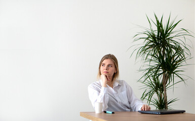 A girl in a white shirt at the office table against the background of a wall with space for text.