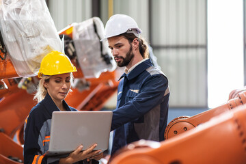 female engineer and chief maintenance technician wearing a safety helmet discussing and examining the operation of a robotic arm. and repairing machinery, equipment parts in a factory.