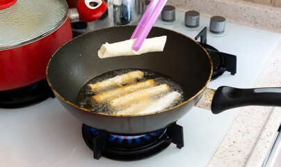 Someone frying Turkish cigarette shaped rolls frying with oil in pan.