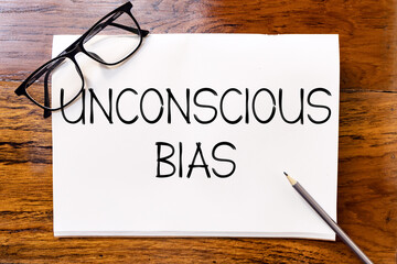 Unconscious bias text on blank notebook paper on wooden table with pencil and glasses aside....