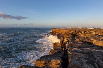 Fototapeta na wymiar Sea waves crash against a rocky cliff at golden hour