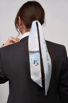 Close-up shot of a young woman with a twilly ribbon in her hair. A brunette girl in a gray jacket with patterned hair band stands with her back on a gray background.