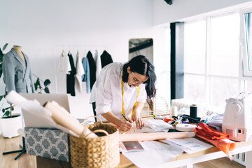 Focused female dressmaker drawing sketches on paper in atelier