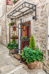 Fototapeta na wymiar Flower vases decorate the entrance to an old stone building in the Old Town of Budva, Montenegro. Vertical view of flower pots at the door in Stari Grad