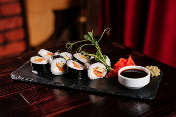 Sushi roll set with ginger and wasabi on black stone with soy sauce side view.