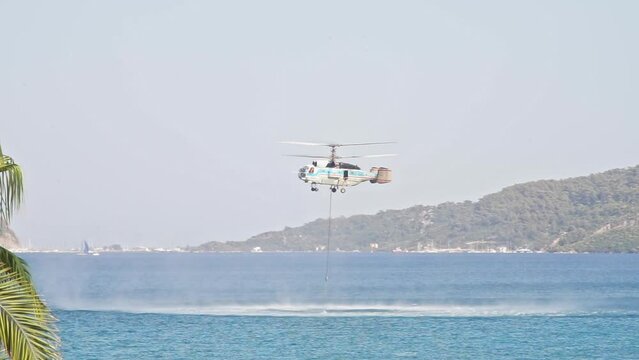 Fire rescue helicopter picks up bambi bucket of water in sea. Process of refilling water bucket and takes off of the sea to extinguish a forest fire