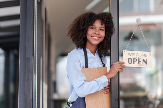 Female store owner or staff, food, cafe or bar, showing the OPEN sign with a welcome smile, welcome. - Powered by Adobe