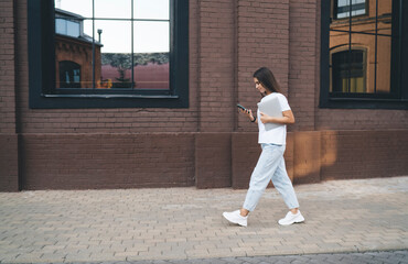 Young woman with smartphone and laptop walking on pavement