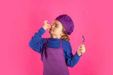 Funny kid chef cook with spoon. Kid chef cook prepares food on isolated studio background. Kids cooking. Teen boy with apron and chef hat preparing a healthy meal.