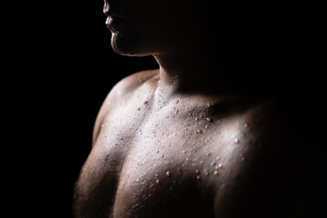 Sweat on skin. Wet sweaty body of a man. Exercise, gym fitness training and sport. Hard workout. Chest and shoulder light, black shadow. Shirtless guy in dark. Shower, sauna or rain. Water drops. - obrazy, fototapety, plakaty