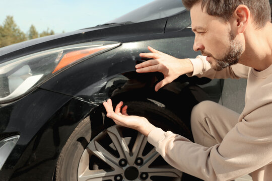 Stressed man near car with scratch outdoors