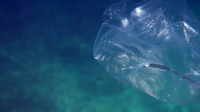 Plastic waste in ocean, underwater shot of a plastic bag drifting in the deep blue sea. Recycling and proper disposal of trash are essential for protecting the environment and wildlife.