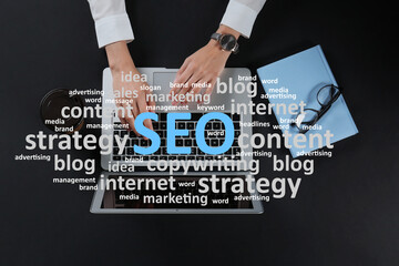 Search engine optimization (SEO). Cloud of words above copywriter with laptop at black table, top...