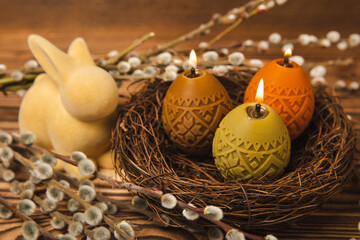 Fototapeta na wymiar Easter candle eggs in a nest on a brown texture table with willow twigs. Easter bunny.Happy easter.Easter candles and spring flower.Spring holiday concept.Copy space.Close-up.