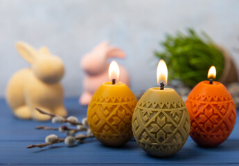 Easter candle eggs in a nest on a blue texture table with willow twigs. Easter bunny.Happy easter.Easter candles and spring flower.Spring holiday concept.Copy space.Close-up.
