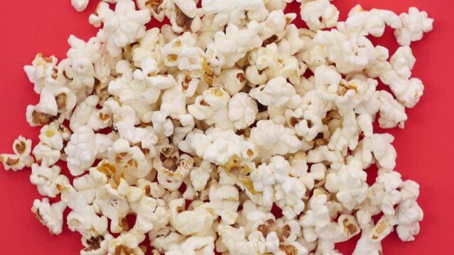 Top view of pile of popcorn on red background revolving, junk food for movies, going out to cinema, entertainment, grains. Close up, 4K Ultra HD.