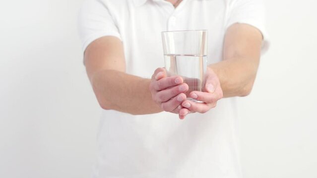 An unrecognizable man in a white T-shirt offers a glass of clean clear water. Concept of friendly help, healthy eating, fitness nutrition