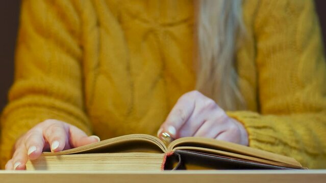A young unrecognizable girl at the table puts a pen between the pages of a book, stops reading, learning, studying, education process and takes a break to rest and relax.