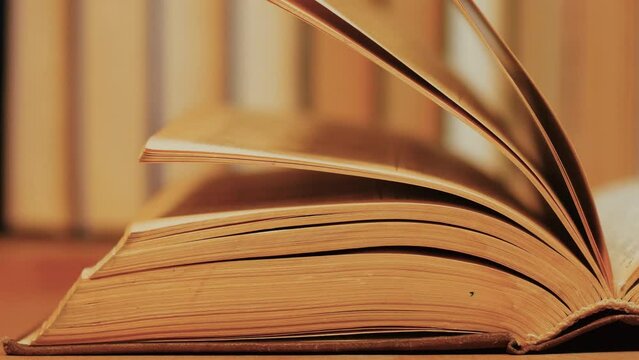 Strong wind flips and turns yellowed pages of an open old vintage book on a table in front of a bookshelf. Concept of reading, education, learning, studying.