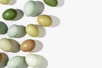 Natural colorful Easter eggs green beige yellow color on white light background, hard Shadow at sunlight. Minimal flat lay frame from Chicken eggs, traditional Easter holiday food, top view
