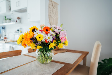 Kitchen counter table with focus on vase with huge multicolor various flower bouquet with blurred background of modern cozy white kitchen. Home interior design details. Mother's day. Copy space.