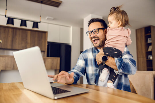 A happy father is working remotely while babysitting his baby girl.