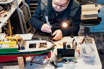 Retired elderly man making ship model building handcraft on the table in his garage. Pensioner...
