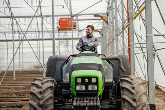 An agronomy worker is plowing the land with tractor in hothouse. - Powered by Adobe