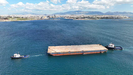 Aerial drone photo of empty barge boat cruising Mediterranean sea assisted by tug boats