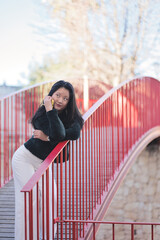 Young Asian girl talking on the phone. The young woman is leaning on the railing of a bridge. Hobby concept.