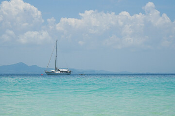Obraz premium The yacht parking in the calm sea with moving paddle boat and mountain with blue sky in background