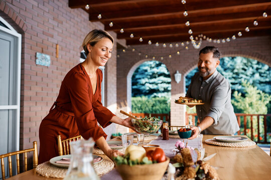 Happy Woman And Her Husband Setting Dining Table For Lunch On Patio.