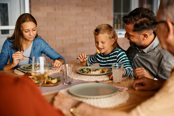 Happy boy eats lunch with his family at dining table on terrace.