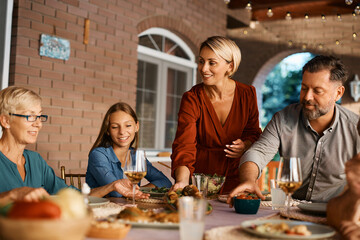 Happy woman serving food at dining table during family lunch on patio.