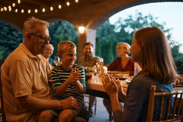 Happy kid and his sister playing clapping game during family dinner on patio.