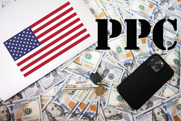 PPC. Pay Per Click concept. USA flag, dollar money with keys, laptop and phone background.