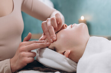 The beautician makes a deep facial massage to a young woman. Face massage technique against aging. Close-up.
