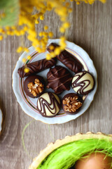 Easter eggs in the basket, bowl of cookies, chocolate pralines, Easter bunny figurine, cups of tea, glasses of juice, flowers and lit candles on the table. Top view.