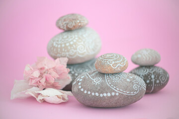 Zen style stacked stones with white line drawings about the universe. there is a pink flower next to the stones on a pink background that transmits calm and tranquility