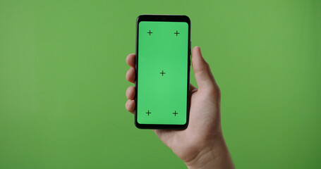 Close up of man's hand holding a smart phone with vertical green mock up chroma key screen and doing gestures on touchscreen 