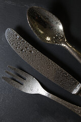 metal cutlery wet with drops of water on a slate table
