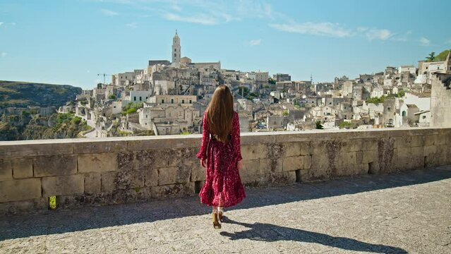 A young woman looking at the gorgeous old town, Sassi di Matera. A female tourist exploring the city on a rocky outcrop with a complex of cave dwellings carved into the mountainside in Matera, Italy.