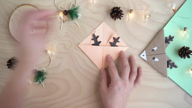 Top view, women's hands make a bookmark out of paper in the origami technique, a craft deer. New Year and Christmas concept. DIY gift wrapping